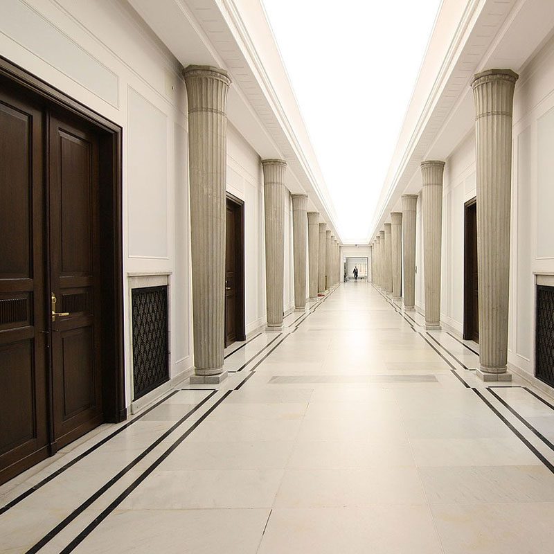 A white hallway with columns and large brown double doors 