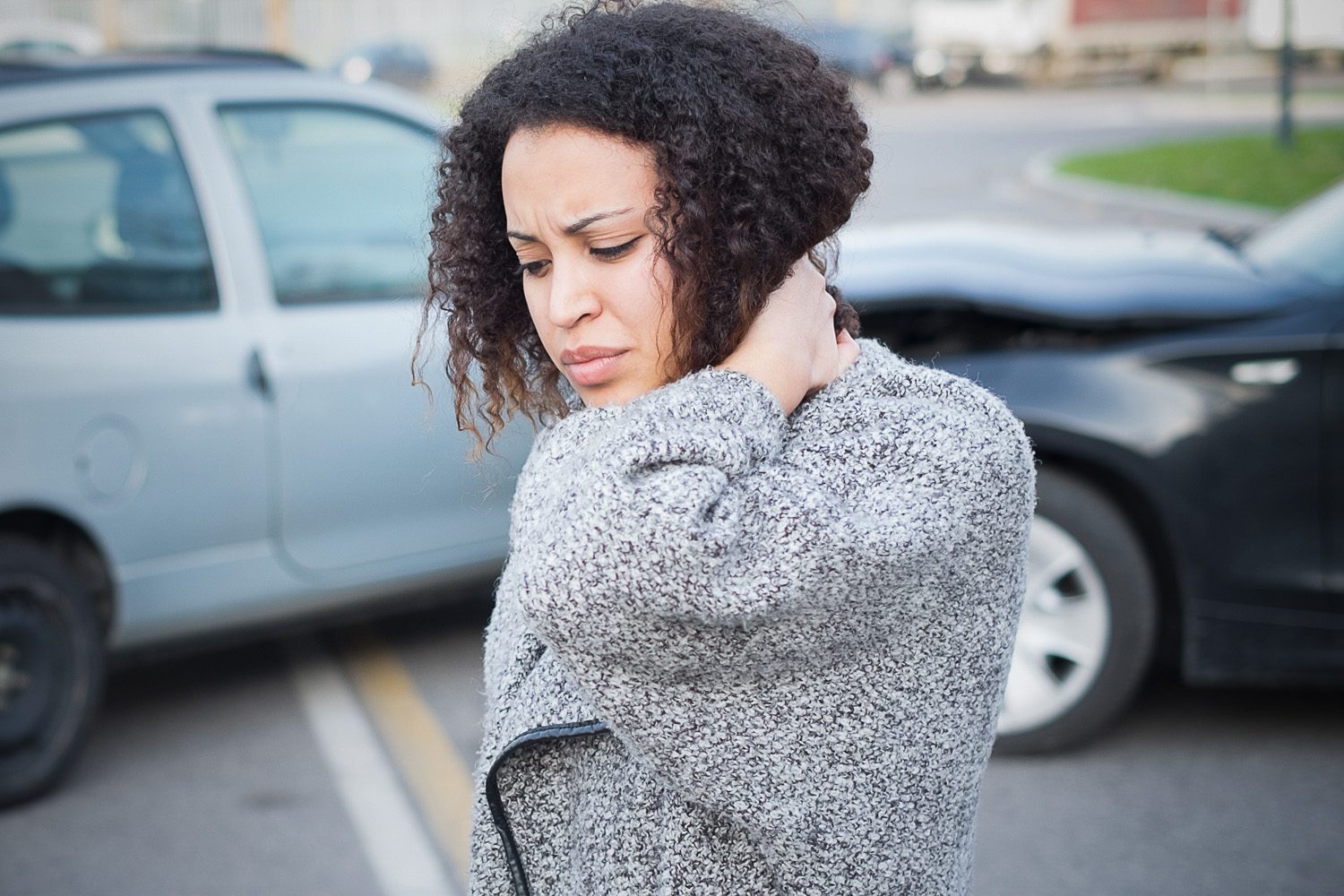 Woman in gray wool jacket holds her neck after a car crash